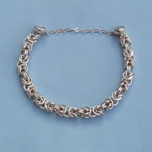 K&ouml;nnte beinhalten: Ein silbernes Kettenarmband mit einem einzigartigen gewebten Design und magnetischen Verschl&uuml;ssen.