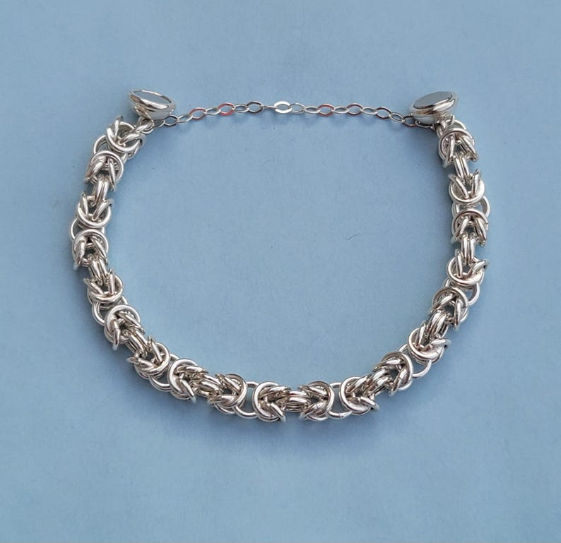 K&ouml;nnte beinhalten: Ein silbernes Kettenarmband mit einem einzigartigen gewebten Design und magnetischen Verschl&uuml;ssen.