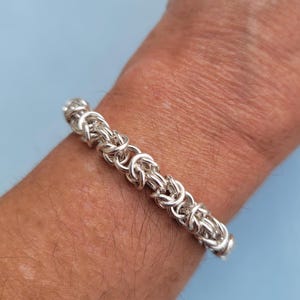 K&ouml;nnte beinhalten: Ein silbernes Kettenarmband mit geflochtenem Design. Das Armband befindet sich an einem Handgelenk.