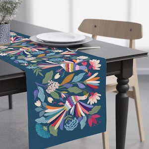 May include: A blue table runner with a colorful floral and bird design. The runner features a repeating pattern of stylized birds with long, colorful tails and flowers in shades of pink, yellow, orange, and green.