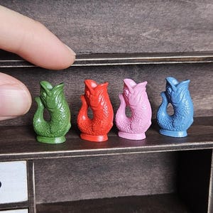 Peut inclure: Quatre figurines de poissons miniatures en vert, rouge, rose et bleu. Chaque petit poisson dressé présente une queue courbée et des écailles détaillées. Ces minuscules objets décoratifs sont alignés sur une étagère avec une finition lisse.