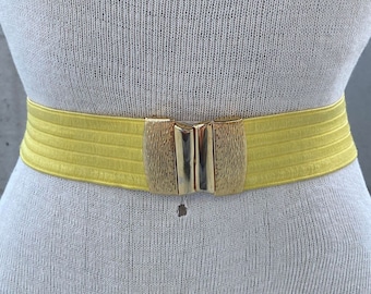 May include: A yellow elastic belt with a gold metal buckle. The belt is made of a stretchy material and has a smooth finish.