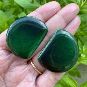 Könnte beinhalten: Ein Paar grüne, halbkreisförmige Ohrringe. Die Ohrringe sind dunkelgrün mit einem schwarzen Zentrum.