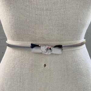 May include: A silver metal belt with a bow-shaped buckle. The belt is on a white mannequin.
