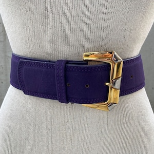 May include: A purple suede belt with a gold and silver buckle. The buckle has a geometric design.