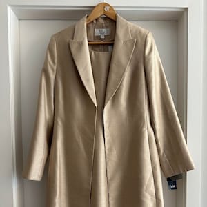 May include: A long, gold-colored jacket with a matching skirt. The jacket has a collar and long sleeves. The skirt is knee-length. The label on the jacket reads "Le Suit".