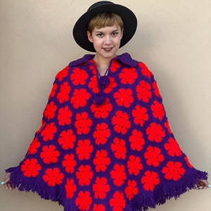 May include: A purple and red crocheted poncho with a fringe border. The poncho has a flower pattern and a tassel tie.
