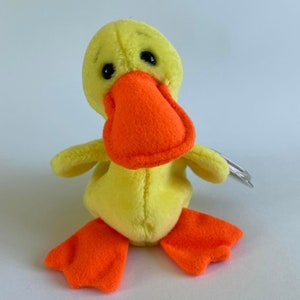 May include: A yellow plush duck with orange feet and beak. The duck has black eyes and a stitched smile.