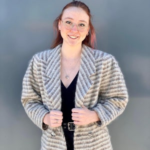 Puede incluir: Un cárdigan a rayas, de manga larga, de doble botonadura, marrón y blanco con un top negro debajo.