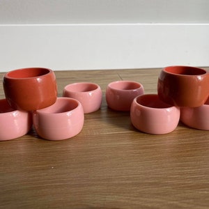 Puede incluir: Un juego de diez anillos para servilletas en dos colores: coral y rosa claro. Los anillos están apilados en forma de pirámide.