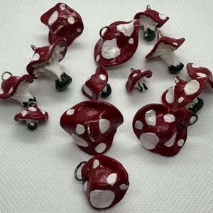 Puede incluir: Una colección de 12 abalorios de setas rojas y blancas con detalles dorados. Las setas están hechas de arcilla polimérica y tienen una variedad de formas y tamaños.