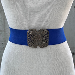 Puede incluir: Un cinturón elástico azul real con una hebilla de filigrana plateada.