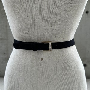 Puede incluir: Un cinturón de ante negro con una hebilla dorada adornada con diamantes de imitación transparentes.