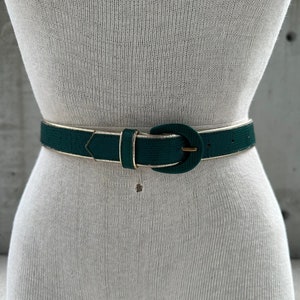 Puede incluir: Un cinturón de cuero verde con una hebilla dorada. El cinturón tiene una superficie texturizada.