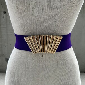 May include: A purple elastic belt with a gold fan-shaped buckle.