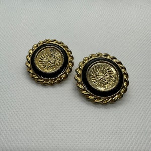 Puede incluir: Un par de pendientes de tono dorado con esmalte negro y un diseño en relieve texturizado en el centro.