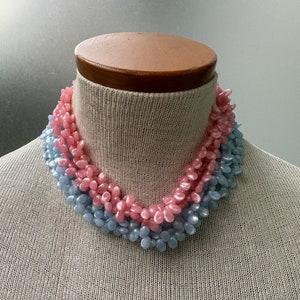 Może przedstawiać: Wielorzędowy naszyjnik wykonany z plastikowych koralików w pastelowych kolorach niebieskim i różowym. Koraliki mają kształt małych, wydłużonych łez.