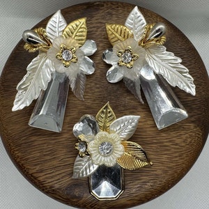 Może przedstawiać: Zestaw trzech srebrnych i złotych kolczyków z białymi perłami i ozdobami ze Swarovskiego. Kolczyki są prezentowane na drewnianej powierzchni.