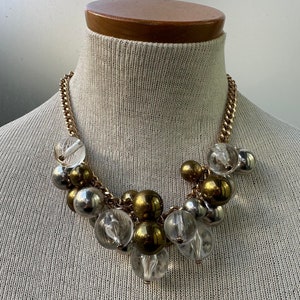 Może przedstawiać: Złoty naszyjnik z łańcuszkiem z przezroczystymi i złotymi koralikami. Koraliki są w różnych rozmiarach i kształtach.