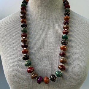 Może przedstawiać: Długi naszyjnik wykonany z kolorowych, okrągłych koralików z złotymi akcentami. Koraliki są połączeniem czerwonego, pomarańczowego, zielonego, czarnego i fioletowego.