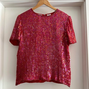 May include: A red sequined top with short sleeves. The sequins are iridescent and create a shimmering effect.