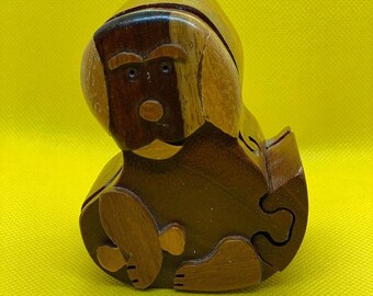 May include: A wooden puzzle box shaped like a dog. The box is made of different shades of brown wood and has a detailed face with black eyes and a brown nose.