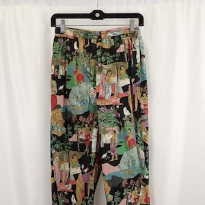 Könnte beinhalten: Schwarze Hose mit einem bunten Druck von Menschen und Tieren. Der Druck zeigt eine Vielzahl von Farben, darunter Grün, Rot, Blau und Gelb.