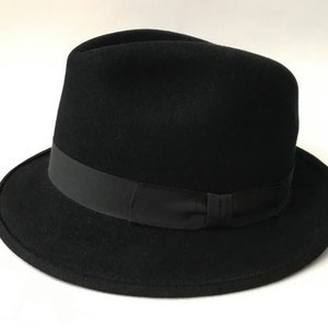 Puede incluir: Un sombrero fedora negro con una cinta negra.
