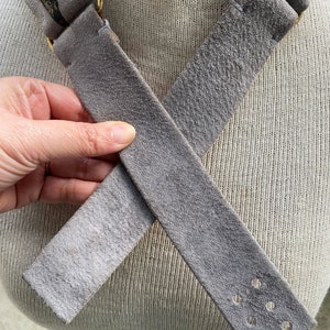 May include: A gray suede strap with a gold metal buckle and a snake skin pattern on one end. The strap has multiple rows of stitching and a row of holes on one end.
