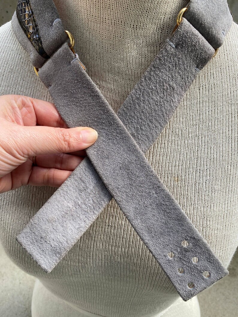 May include: A gray suede strap with a gold metal buckle and a snake skin pattern on one end. The strap has multiple rows of stitching and a row of holes on one end.