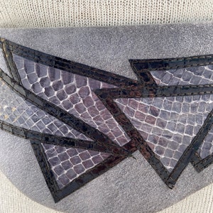 May include: A gray leather belt with a geometric design made of black and purple snakeskin. The belt is stitched with black thread.