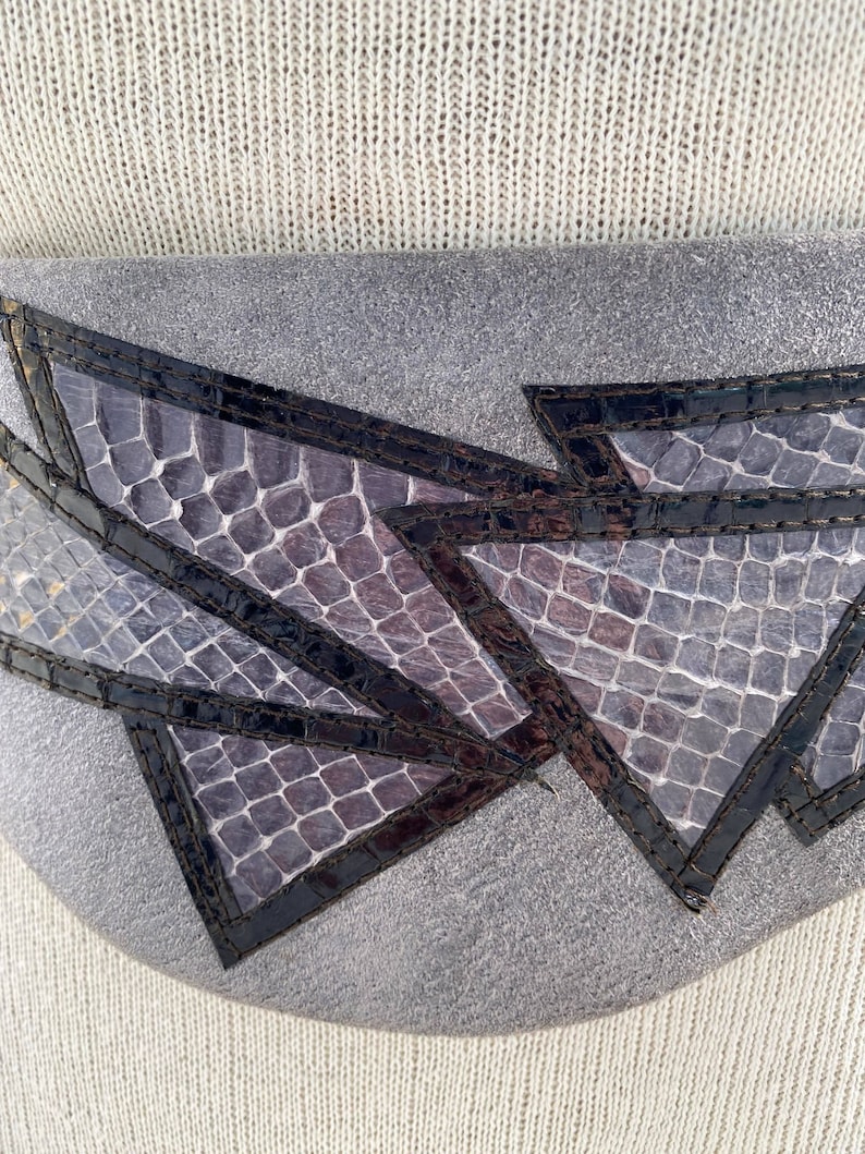 May include: A gray leather belt with a geometric design made of black and purple snakeskin. The belt is stitched with black thread.
