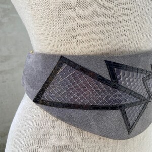 May include: A gray suede belt with black leather accents and a geometric design. The belt features a snakeskin pattern in the center.