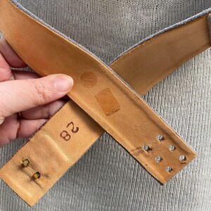May include: A brown leather belt with a buckle and a size 28 stamped on the back.