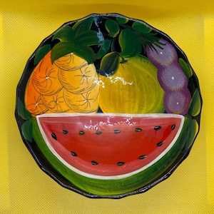 Może przedstawiać: Czarna ceramiczna miska z ręcznie malowanym wzorem owoców. Miska przedstawia arbuza, ananasa, winogrona i żółty owoc. Miska idealnie nadaje się do serwowania owoców lub przekąsek.