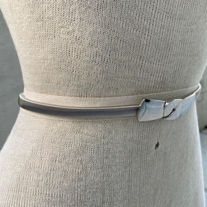May include: A silver stretchy belt with a silver buckle. The belt is on a white mannequin.