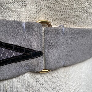 May include: A gray suede belt with a gold metal buckle and a black and gray snakeskin pattern on the front.