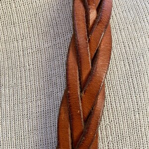 May include: Close-up of a brown leather braided belt. The leather is woven in a tight, intricate pattern.