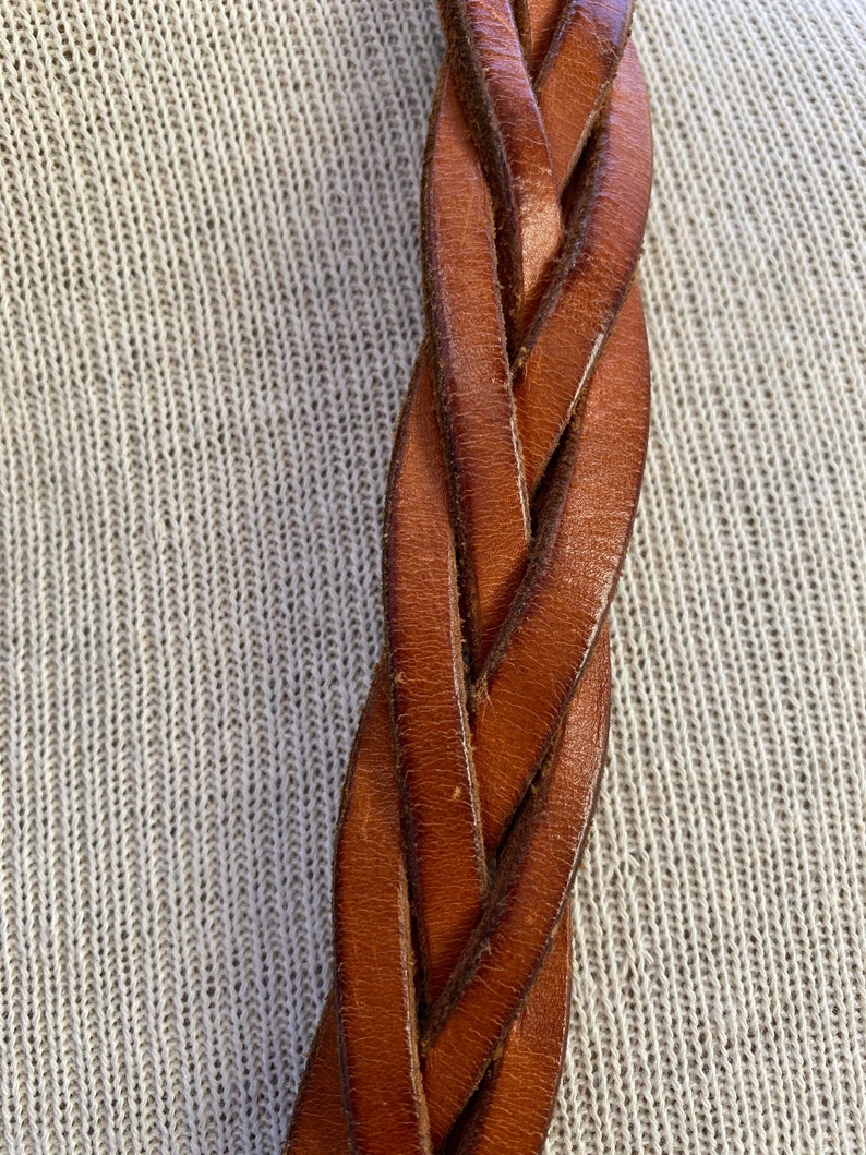 May include: Close-up of a brown leather braided belt. The leather is woven in a tight, intricate pattern.
