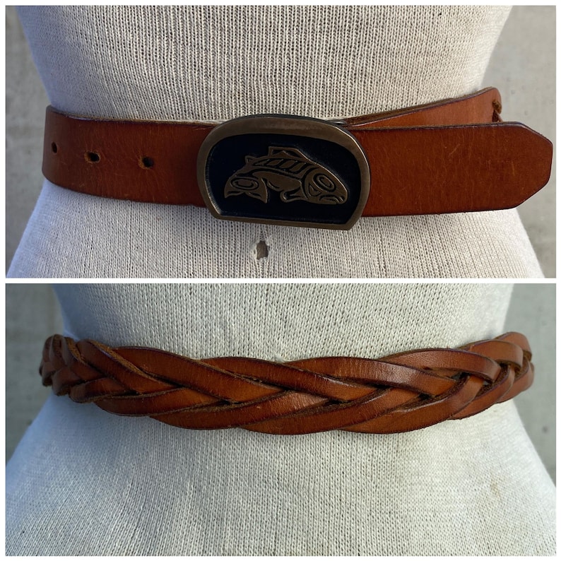 May include: Two brown leather belts with different buckle styles. The top belt has a large, ornate buckle with a fish design. The bottom belt is braided and has a simple buckle.