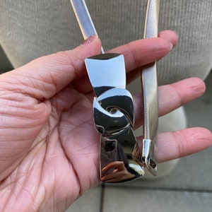May include: A silver metal belt with a stretchy, coiled design and a large, silver, abstract buckle.