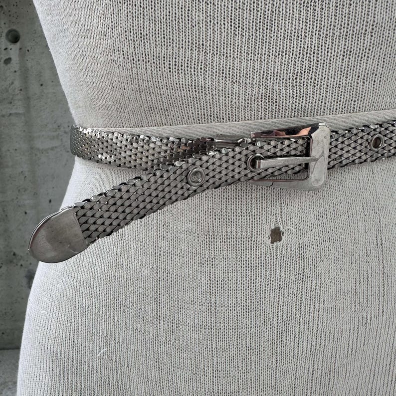 Peut inclure: Une ceinture en maille argent&eacute;e avec une boucle rectangulaire et une pointe assortie. La ceinture est pr&eacute;sent&eacute;e sur un mannequin, mettant en valeur son design tiss&eacute; et son &eacute;clat m&eacute;tallique. Un accessoire &eacute;l&eacute;gant.