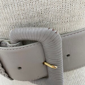 Puede incluir: Un cintur&oacute;n de cuero gris con una hebilla texturizada. La hebilla es de forma rectangular simple con un cierre dorado.