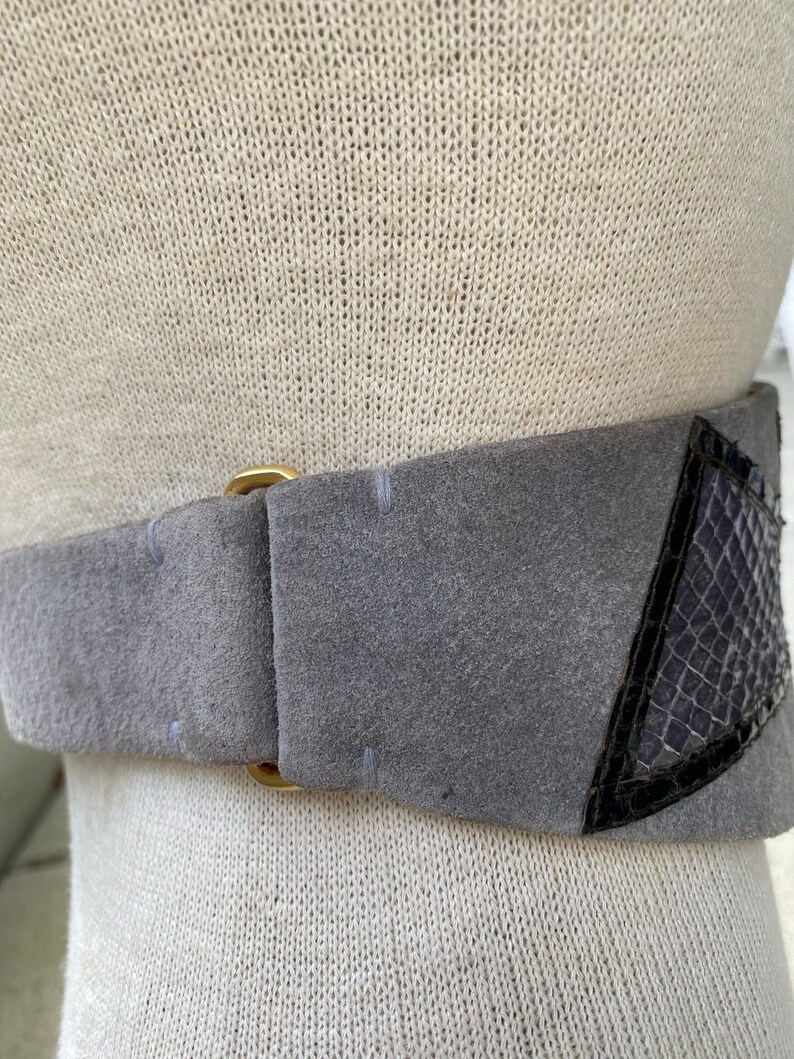 May include: A gray suede belt with a gold buckle and a black snakeskin detail.