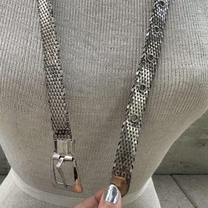 Peut inclure: Une ceinture en m&eacute;tal argent&eacute; avec un motif en maille. La ceinture a une boucle rectangulaire et des accents circulaires. La ceinture est pr&eacute;sent&eacute;e sur un mannequin.
