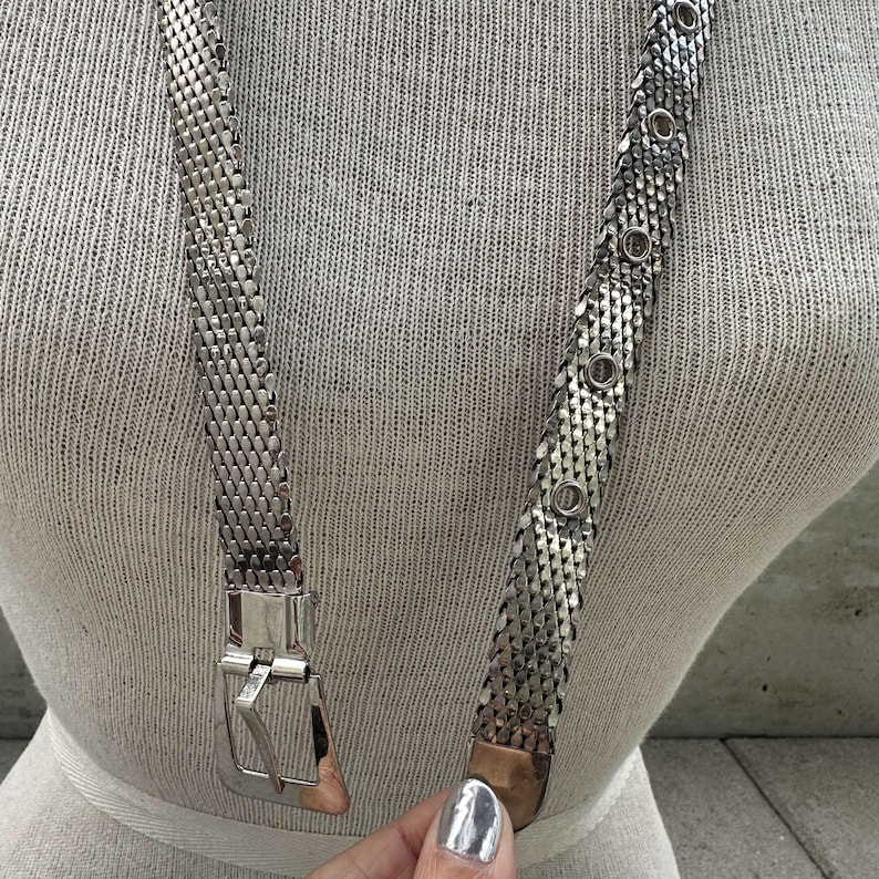 Peut inclure: Une ceinture en m&eacute;tal argent&eacute; avec un motif en maille. La ceinture a une boucle rectangulaire et des accents circulaires. La ceinture est pr&eacute;sent&eacute;e sur un mannequin.