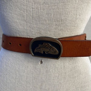 May include: A brown leather belt with a large, oval-shaped buckle featuring a stylized fish design in black and gold.