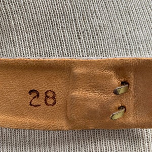 May include: Close-up of a brown leather belt with a brass buckle. The belt is labeled with the number "28".