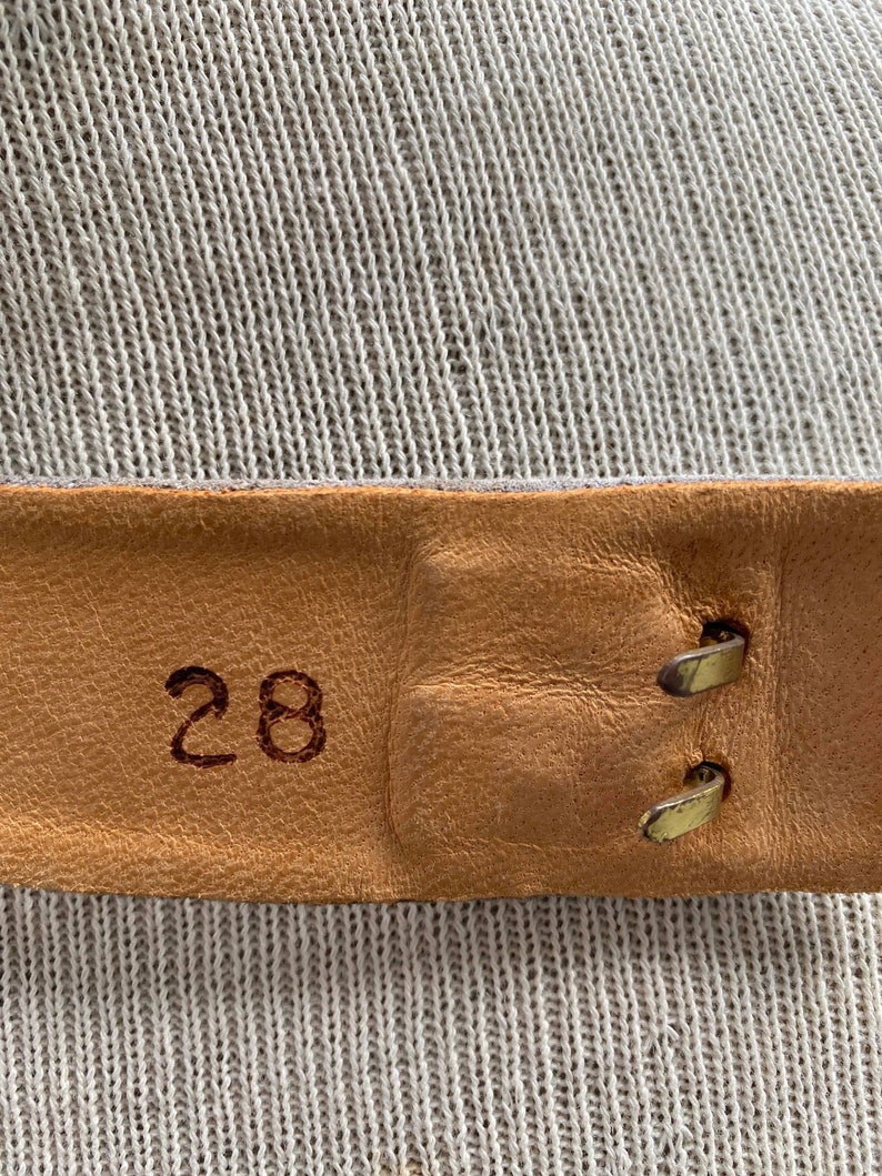 May include: Close-up of a brown leather belt with a brass buckle. The belt is labeled with the number "28".