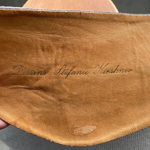 May include: Close-up of a brown leather patch with the text "Versace Stefanie Kostenko" written in black ink.